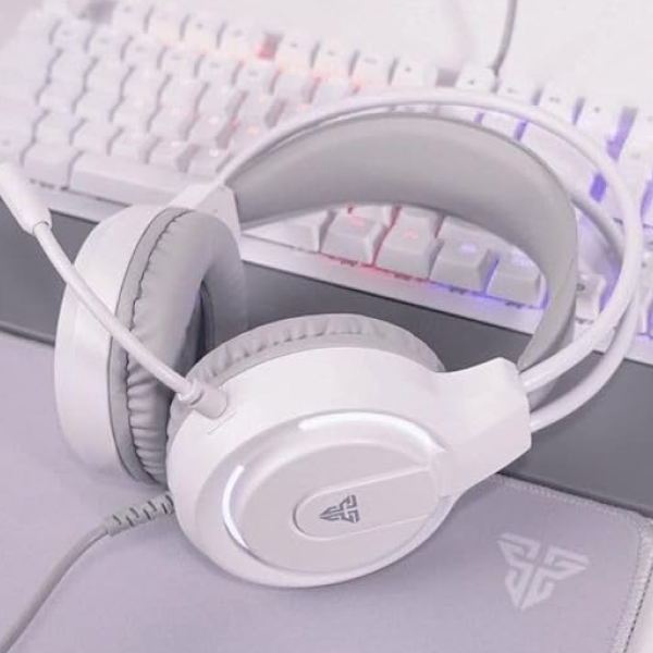 White over-ear gaming headset with a flexible microphone, shown resting on a desk in front of a white mechanical keyboard with RGB backlighting.