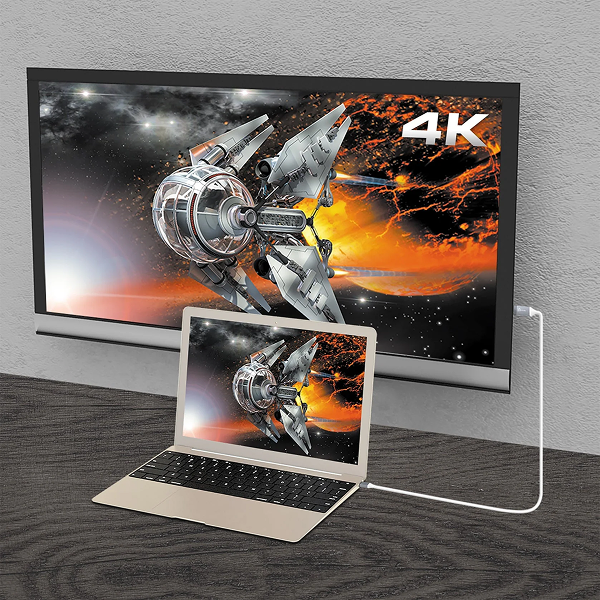 j5create JCC153G USB-C to 4K HDMI Cable - DokkanTech A 4K monitor displaying a futuristic spaceship scene, shown connected to a laptop on a dark wood surface against a light gray wall.
