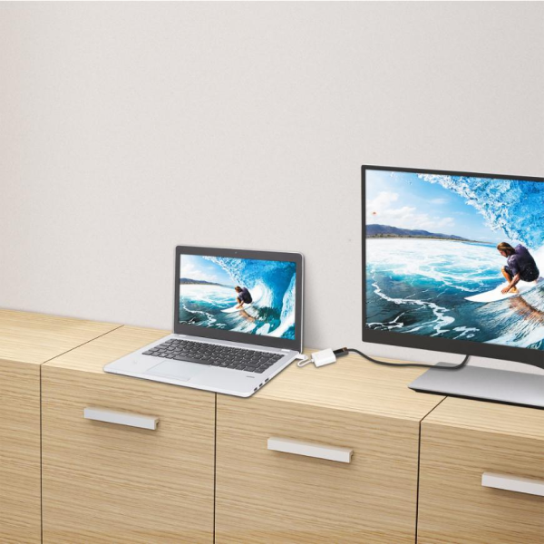 j5create JDA154 DisplayPort to HDMI Adapter A desktop monitor and laptop sit on a light wood cabinet against a plain off-white wall. The laptop is open and the monitor is also on, displaying a surfing scene on screen.