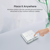 A wireless four-button wall switch shown on a light gray tabletop, with a person's finger touching one of the switches. Text at the top reads 'Place It Anywhere' and 'Wireless switch can be carried around home or attached to any surface without cables.