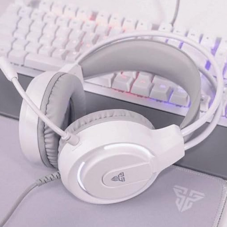 White over-ear gaming headset with a flexible microphone, shown resting on a desk in front of a white mechanical keyboard with RGB backlighting.