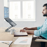 j5create JTS127 Multi-Angle Laptop Stand Designed to fit mostl aptops up to 16 inches - DokkanTech  Man sitting at a desk using a laptop with a stand, in a bright room.