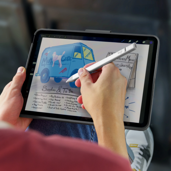 A person holding a tablet with a silver stylus, writing on the screen. The tablet is shown in a close-up, with the person's hands and torso visible against a blurred background.