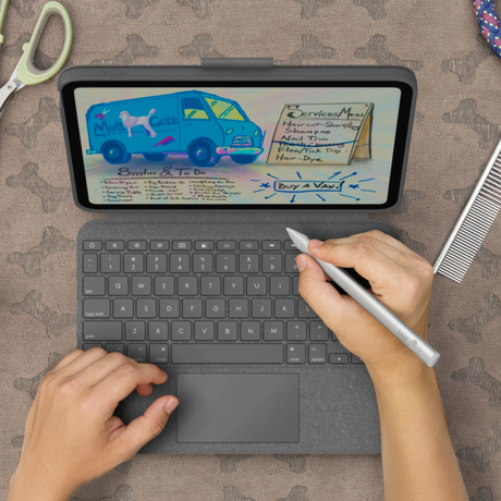 A top-down view of a person using a tablet with a dark gray keyboard case and stylus on a patterned fabric surface. The tablet screen shows a handwritten-style menu and notes, including 'Mule Cut' and 'Services Menu'.
