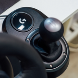 Close-up of a black Logitech racing simulator gear shift knob and console with a visible Logitech logo, set against a blurred background.