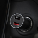 Close-up of a black 2-port USB car charger plug with one USB-A port and one USB-C port, set into a dark car cigarette lighter socket.