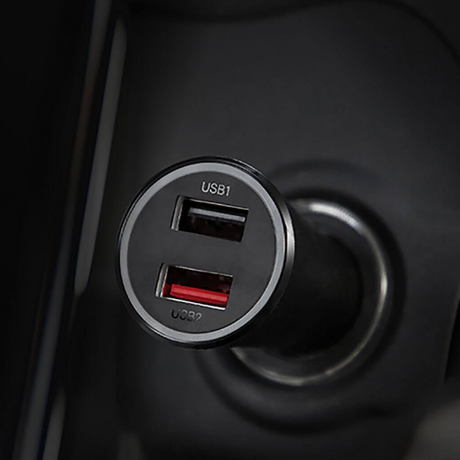 Close-up of a black 2-port USB car charger plug with one USB-A port and one USB-C port, set into a dark car cigarette lighter socket.