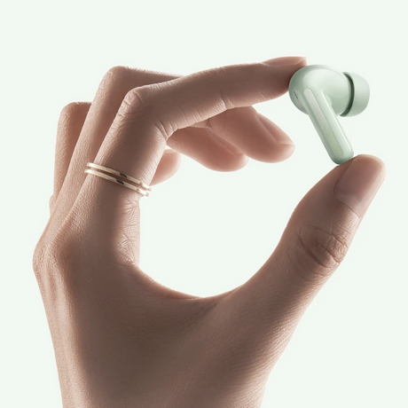 A close-up of a hand holding a small mint green wireless earbud against a bright white background.
