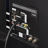Close-up of the rear panel of a black electronic device showing various video and audio input ports, including HDMI, LAN, USB, RCA jacks, and antenna connectors, with a black cable plugged into the HDMI port.