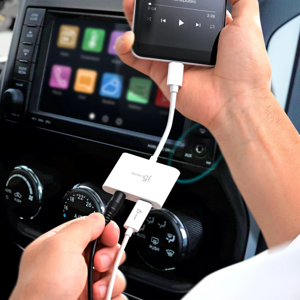 A close-up of a person's hands using a white 3-in-1 USB adapter to charge a smartphone and another device in a car. The adapter is labeled with the brand 'JYP'.
