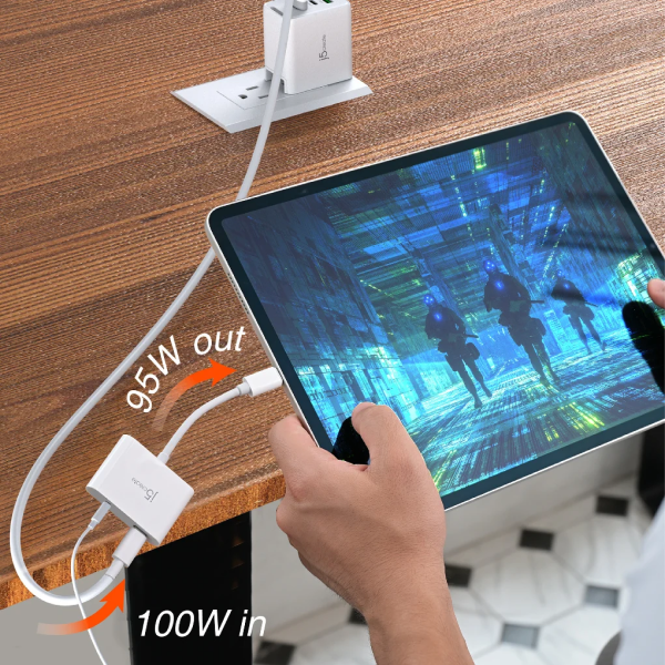 A hand holds a tablet connected to a white multi-port charger plugged into a wooden wall outlet. The charger supplies 95W output while receiving 100W input from the tablet screen, with orange arrows and text indicating power flow.