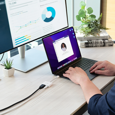 Person using a laptop with a monitor displaying graphs and charts on a desk.