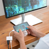 Person using a smartphone with a USB hub connected to a computer monitor on a desk.