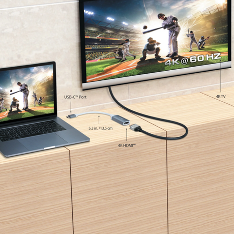 Laptop connected to a TV via USB-C and HDMI cables, displaying a sports game.