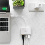 j5create JCA351USB - Cto 4K HDMI Ethernet Adapter - DokkanTech A white J5selects USB hub connected to a laptop on a white marble desk, with a small potted succulent and a wall outlet in the background.