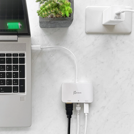 j5create JCA351USB - Cto 4K HDMI Ethernet Adapter - DokkanTech A white J5selects USB hub connected to a laptop on a white marble desk, with a small potted succulent and a wall outlet in the background.