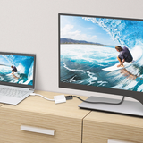 j5create JDA158 DisplayPort to 4K HDMI Active Adapter Two screens displaying a surfer on a wave, one larger and one smaller, on a wooden desk.