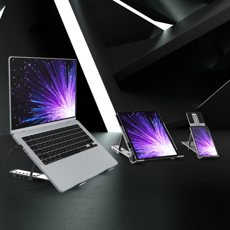 A silver laptop, tablet, and smartphone arranged on a dark tabletop with angled black geometric background panels. The screens all display a purple and blue burst wallpaper.