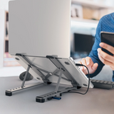 Laptop on a stand with a person using a smartphone in an office setting