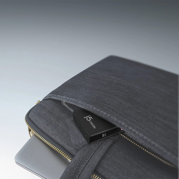 A dark gray fabric laptop sleeve with gold-tone zippers, shown holding a black JSDigital USB drive, photographed on a clean gray gradient background.