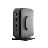A compact square electronic device with rounded corners, shown in a three-quarter view on a white background. The device has a dark gray front face with a circular dial, a black side panel with ports, and a black stand.