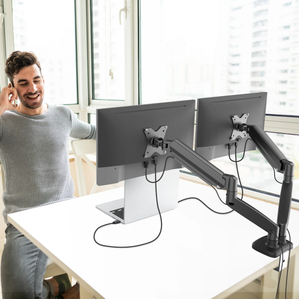 Man using a computer setup with dual monitors on an adjustable arm in a bright room.