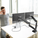 Man using a computer setup with dual monitors on an adjustable arm in a bright room.
