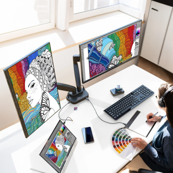 Person working at a desk with multiple monitors displaying colorful artwork.