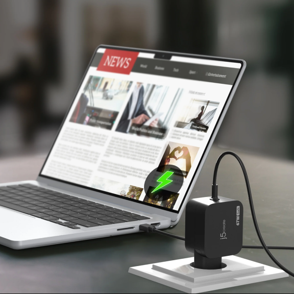 A black GTRUN 15W laptop charger on a white charging stand, connected to a silver laptop on a dark desk with a blurred indoor background.