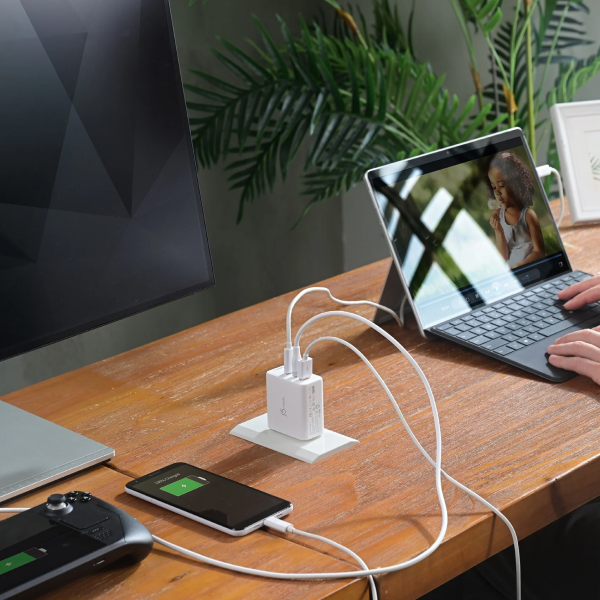 Desk setup with multiple electronic devices being charged using a power strip, including a laptop, phone, and gaming console.