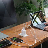 Desk setup with multiple electronic devices being charged using a power strip, including a laptop, phone, and gaming console.