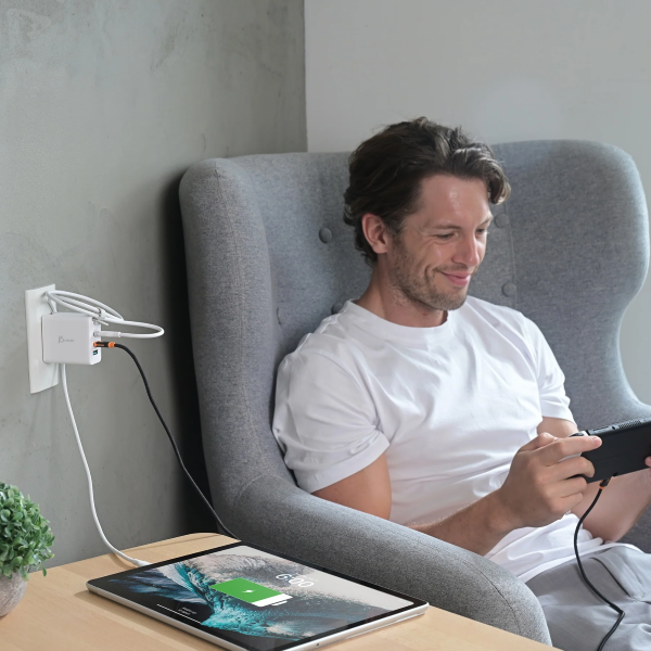 Man sitting in a modern chair using a smartphone with a tablet on a table beside him.