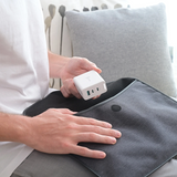 Person holding a white power adapter next to a gray laptop on a couch.