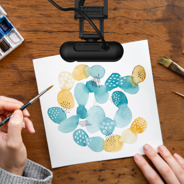 Person painting a colorful design on paper with a lamp illuminating the work area.